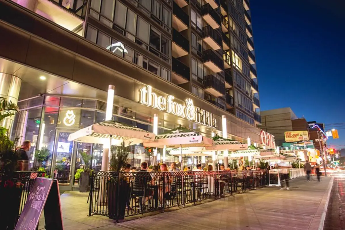 Fox on John at night. The Fox and Fiddle storefront on John Street with patio diners under Heineken umbrellas.