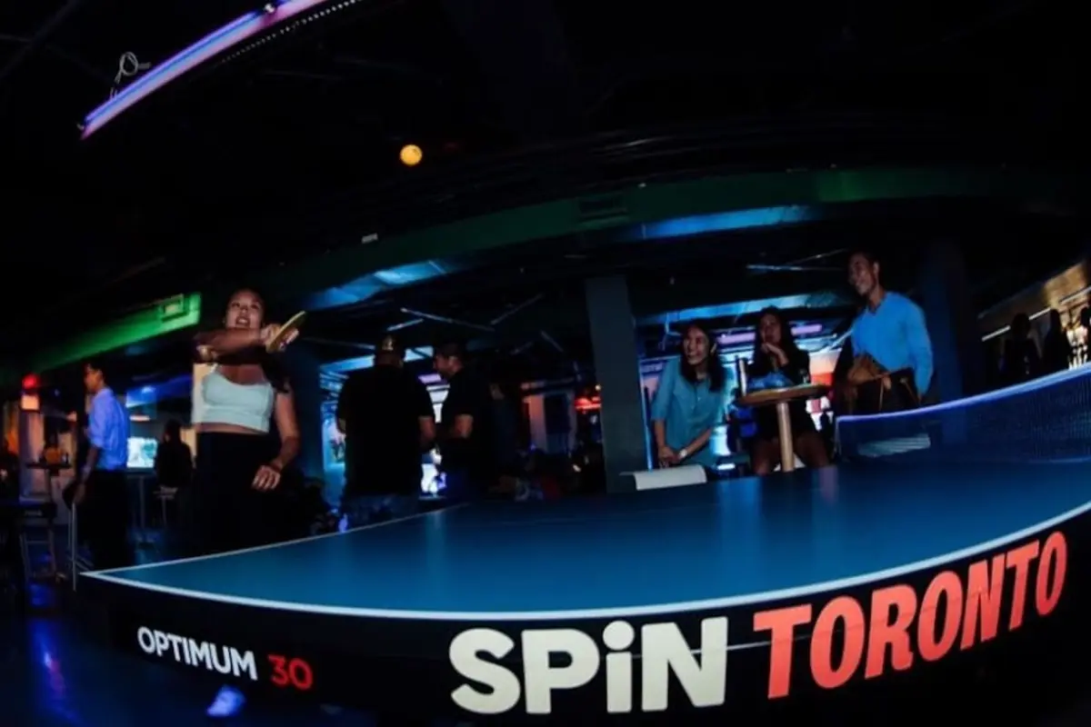Inside Spin Toronto. Player at the blue ping-pong table with SPiN TORONTO branded type along the table edge.