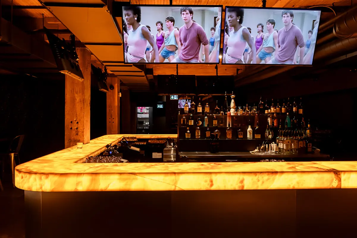 Inside Sunrise Forgives on King West. Glowing onyx bar under wood-paneled ceiling with overhead TV screens.